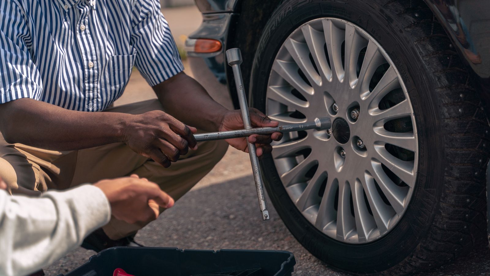 Adult teaching a teenager how to change a car tire