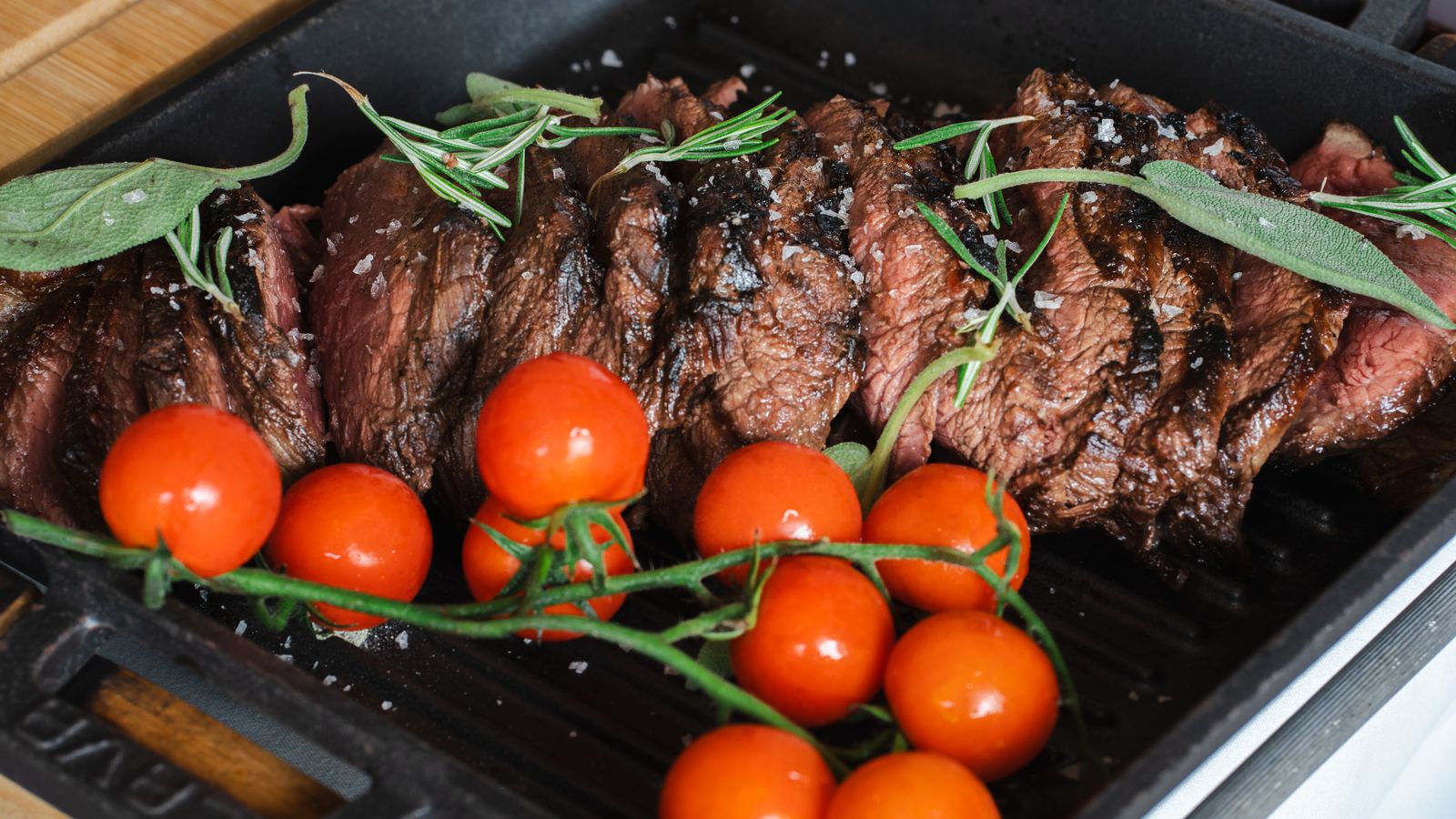 Sliced grilled steak showing the interior doneness beside rosemary and tomatoes