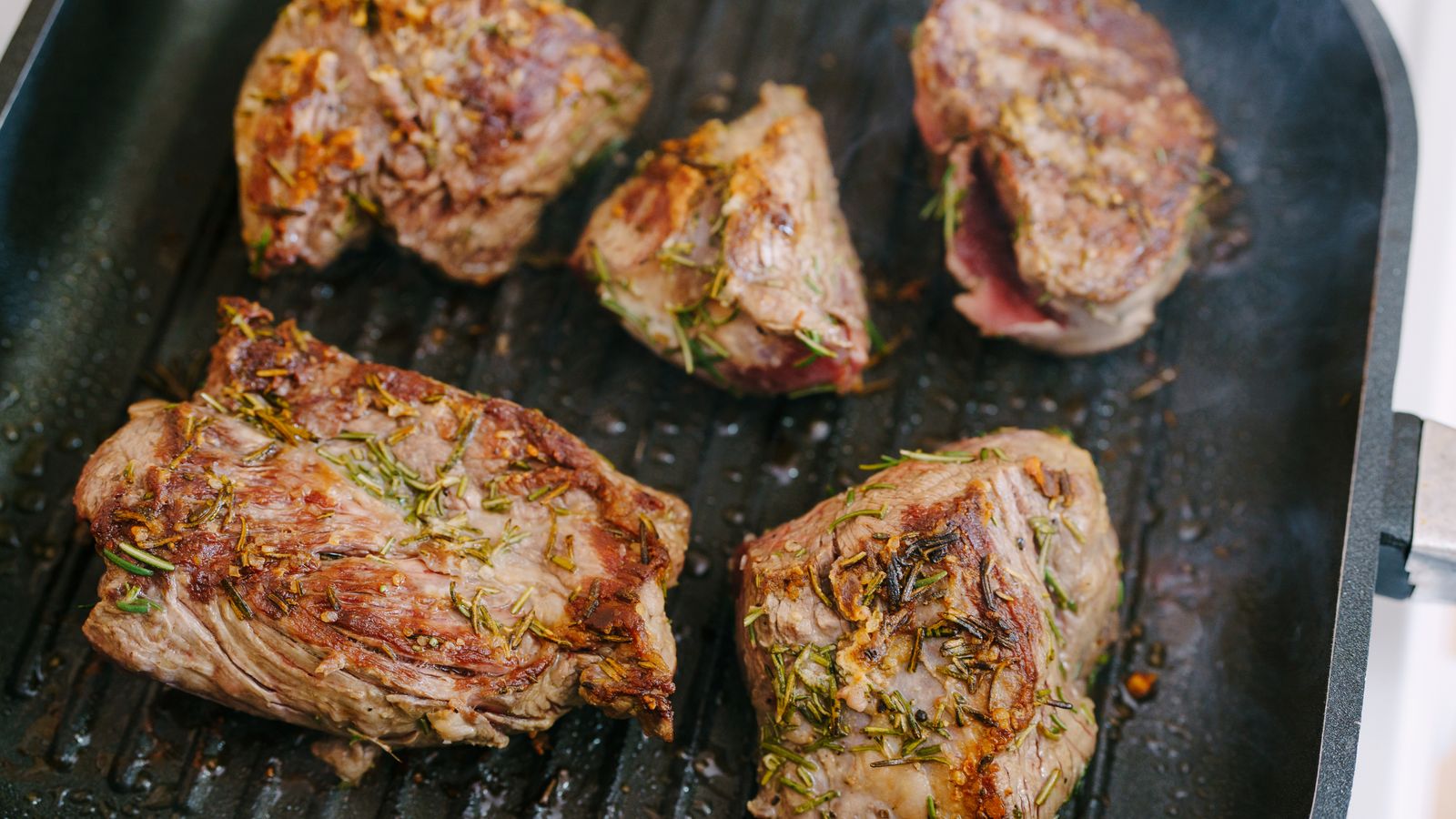 Seasoned meat and fresh herbs prepared beside a grill pan