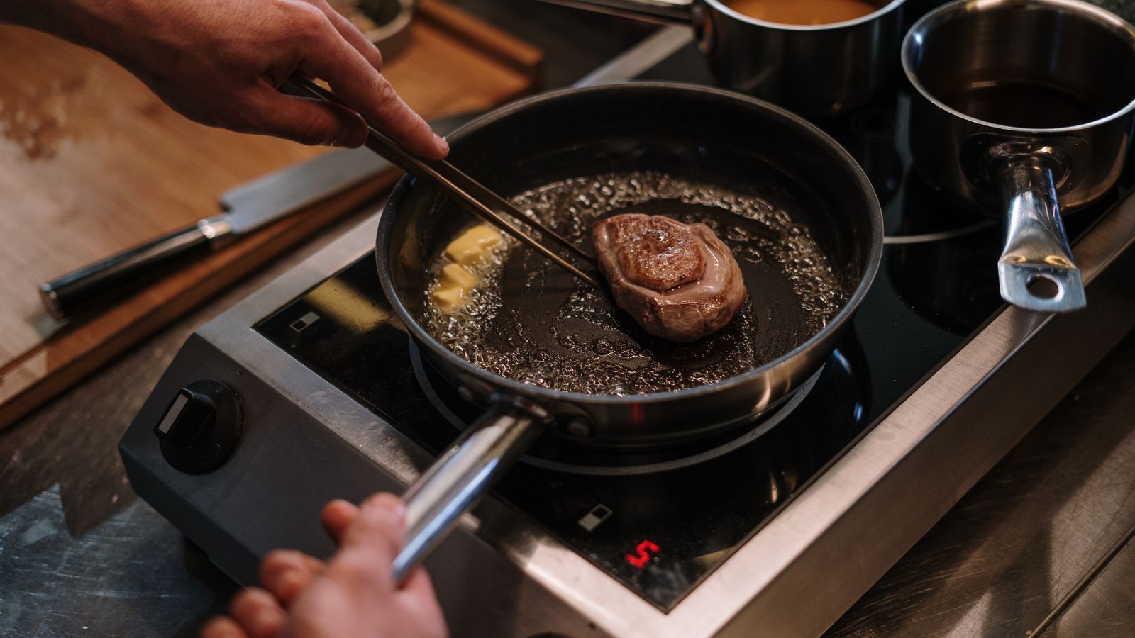 Hands turning and basting a pan-seared steak on the stove
