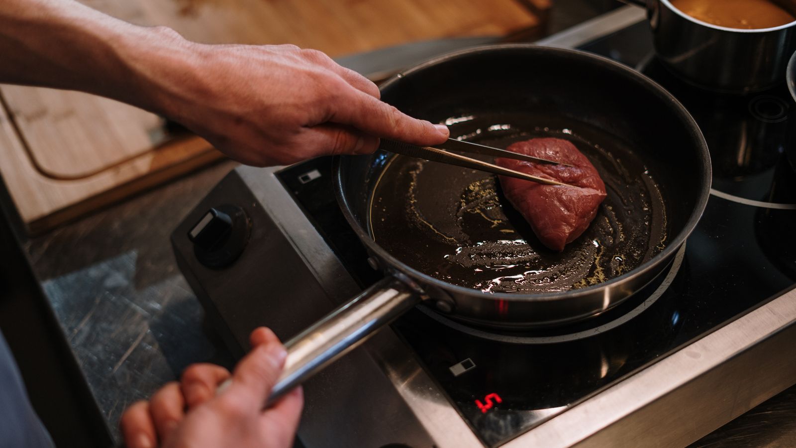 Chef controlling a steak with tongs while searing in a skillet