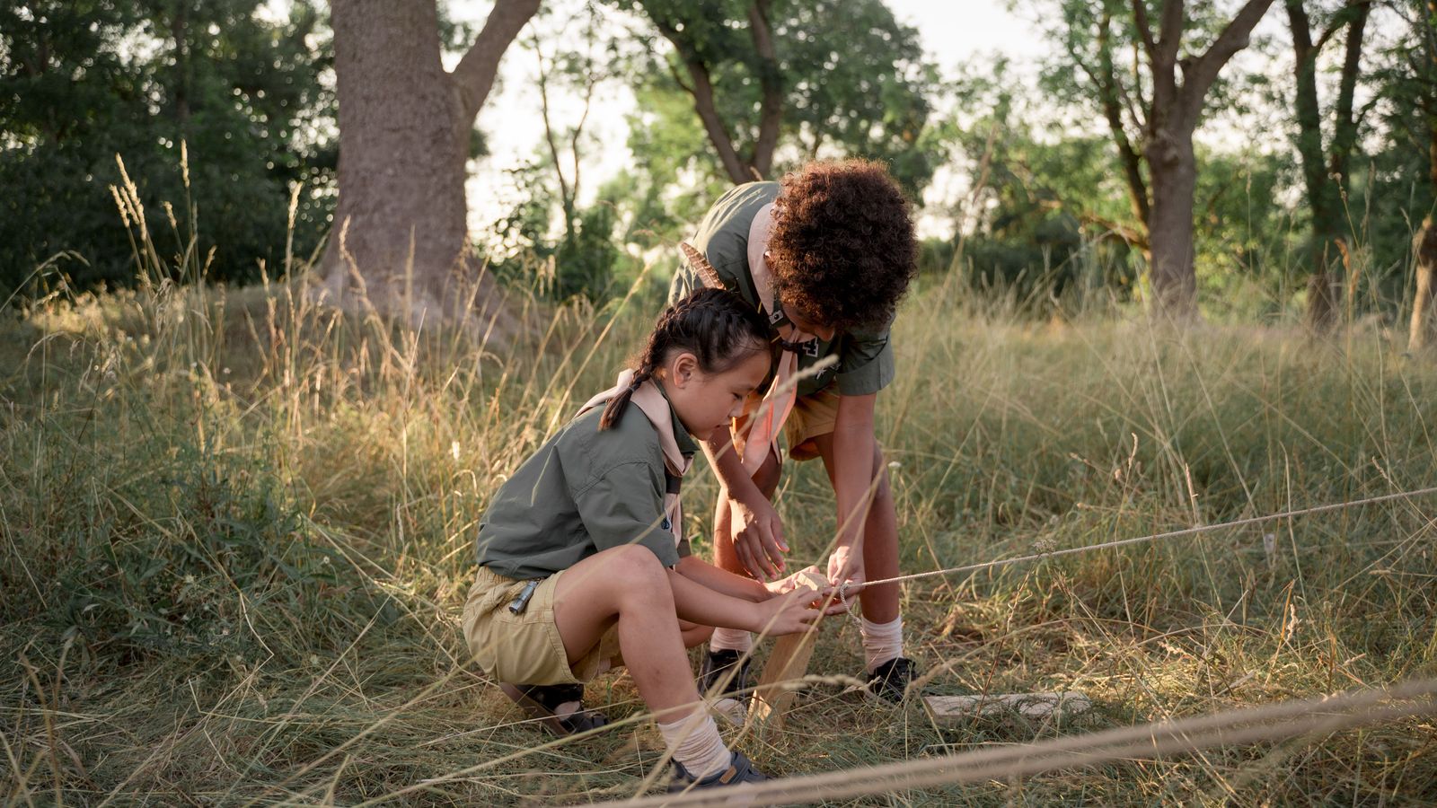 Two scouts practicing rope knots at a grassy campsite