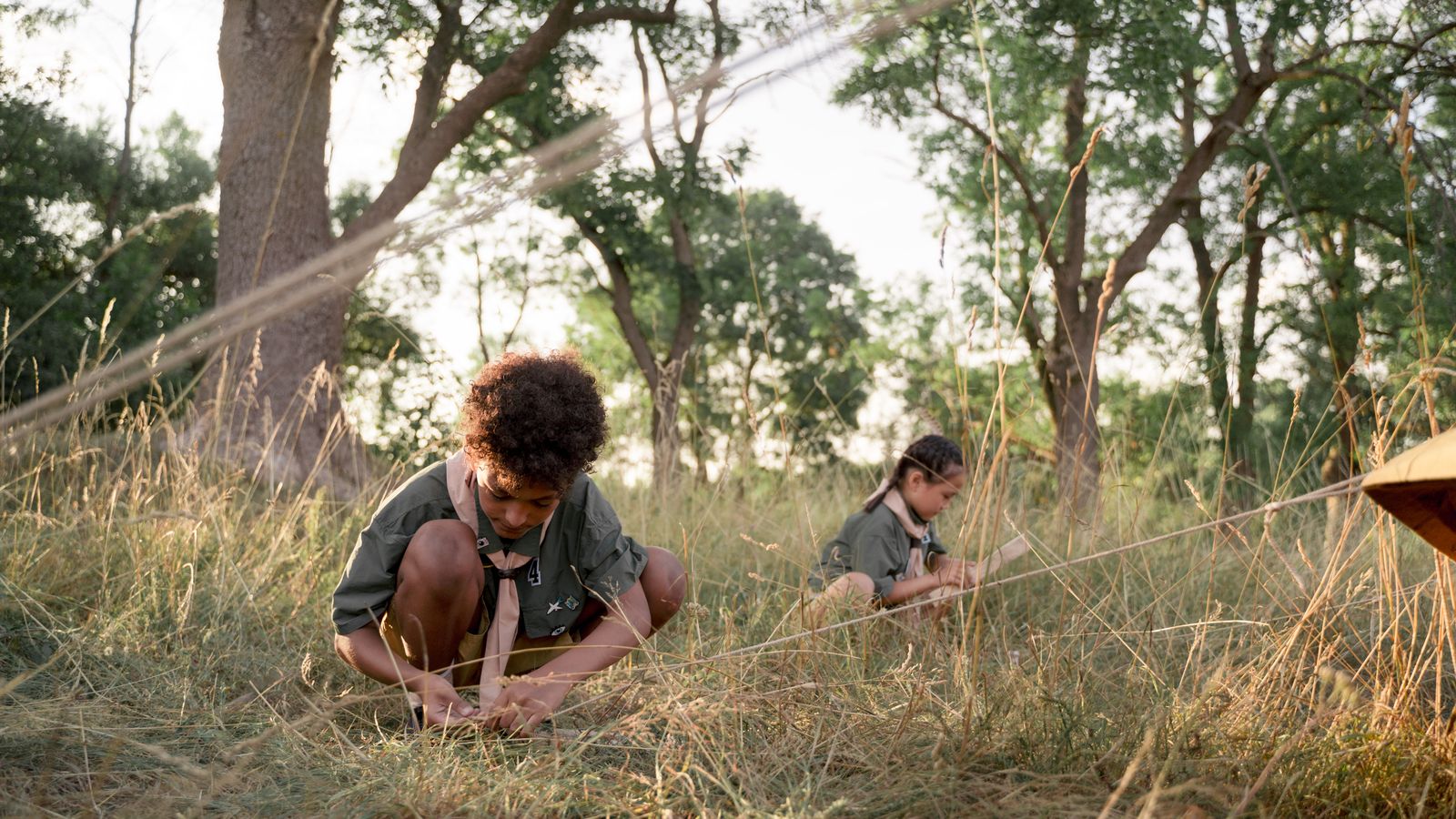 Two young campers setting up a tent in a forest clearing